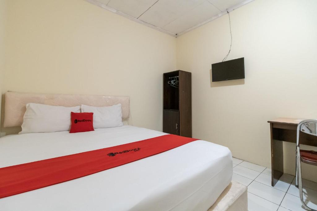 1 dormitorio con cama blanca y almohada roja en RedDoorz Syariah At Jalan Raflesia Nusa Indah Bengkulu en Bengkulu