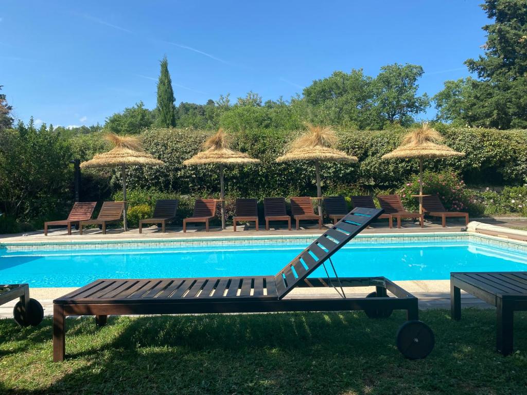 a swimming pool with chairs and umbrellas and a bench at GITE LES GRANDES VIGNES, SUD Ardèche, indépendant et privatisé, piscine chauffée, climatisation, SPA, 11 chambres, 8 salles de bains in Sanilhac