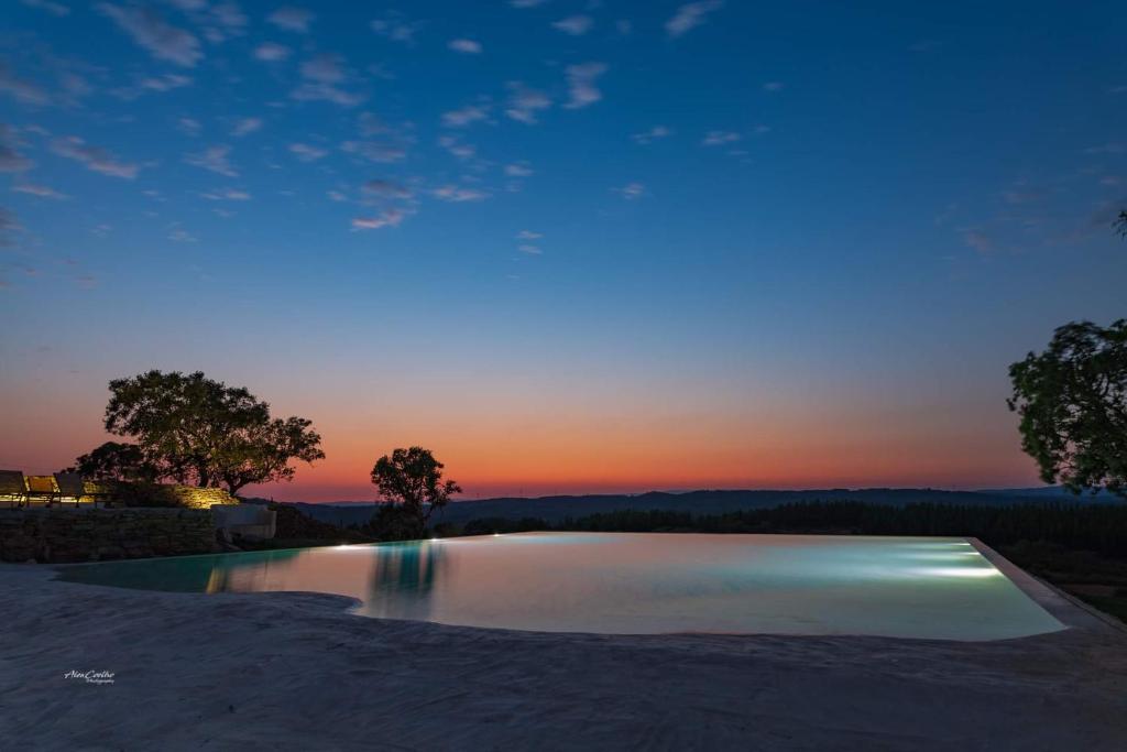 una piscina de agua con una puesta de sol en el fondo en Chão da Velha - Casas de Campo en Nisa