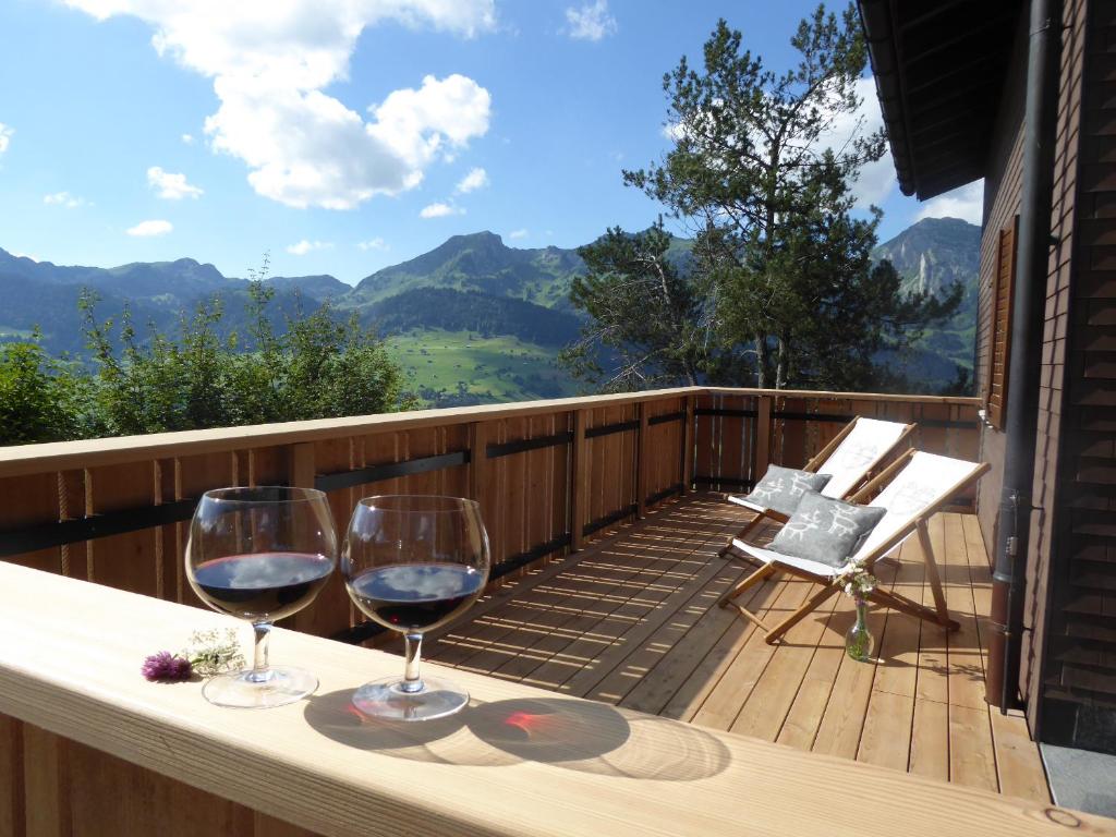 dos copas de vino en una terraza con montañas en el fondo en Ferienhaus Oberguet, en Unterwasser