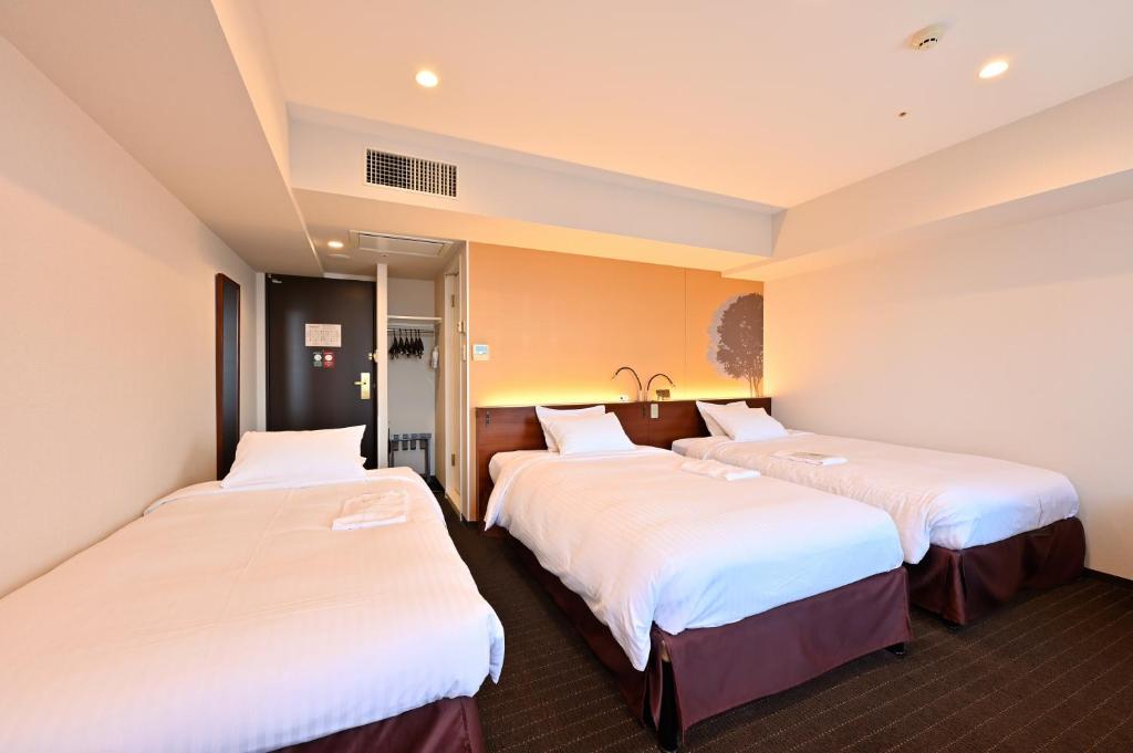 duas camas num quarto de hotel com lençóis brancos em Hotel Keihan Sapporo em Sapporo
