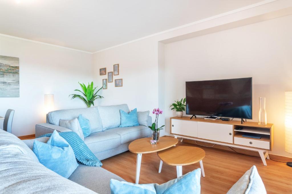 ein Wohnzimmer mit einem blauen Sofa und einem Flachbild-TV in der Unterkunft Privilege Apartment Dalia with Rooftop Pool, Village Marina - Olhão in Olhão