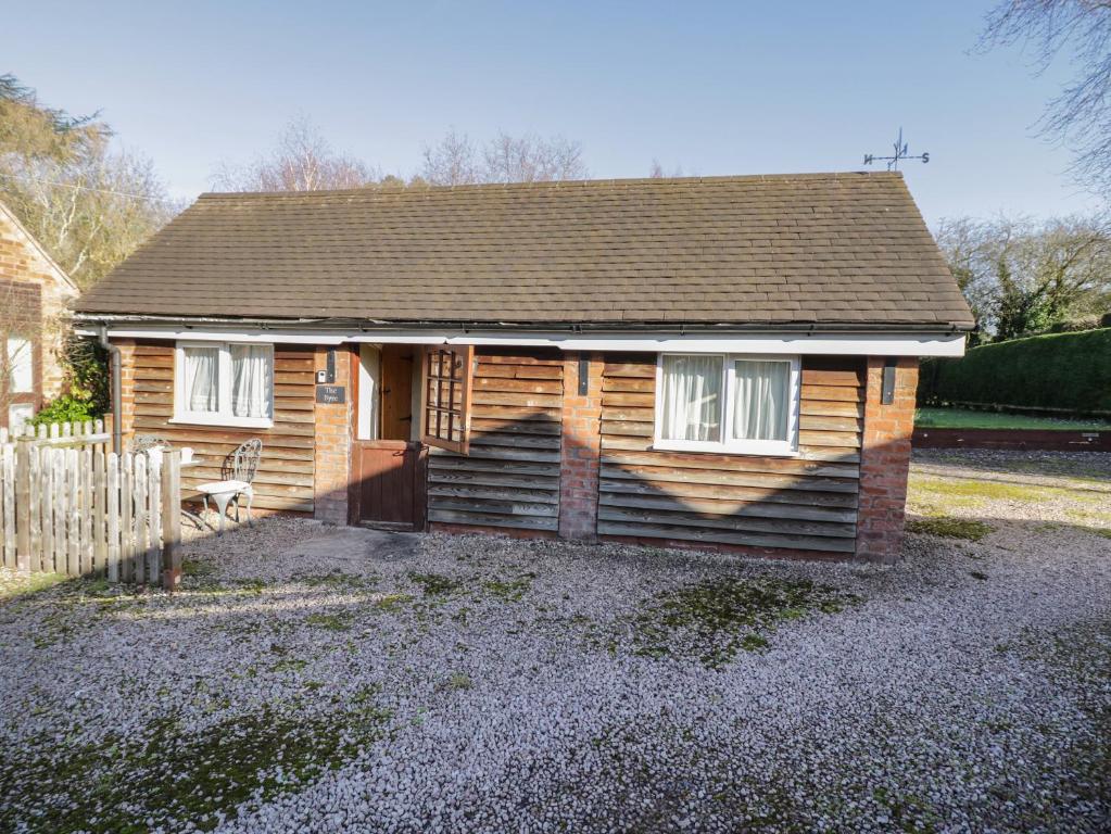 uma cabana de madeira com duas janelas e uma cerca em The Byre em Worcester