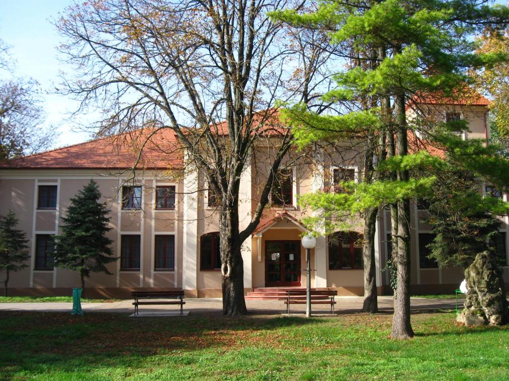 a building with trees in front of it at Kaštel Hotel in Bačka Topola