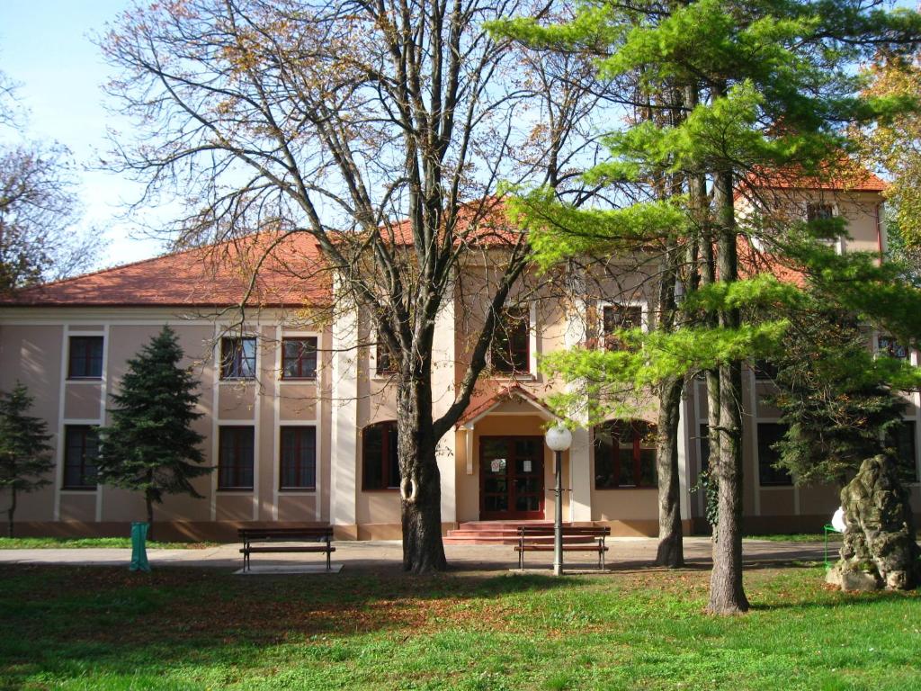 un edificio con árboles delante de él en Kaštel Hotel en Bačka Topola