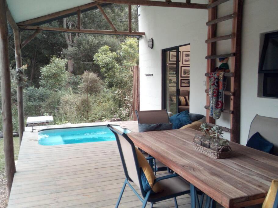 une table et des chaises en bois sur une terrasse avec piscine dans l'établissement Plettenberg Bay Cottage, à Plettenberg Bay