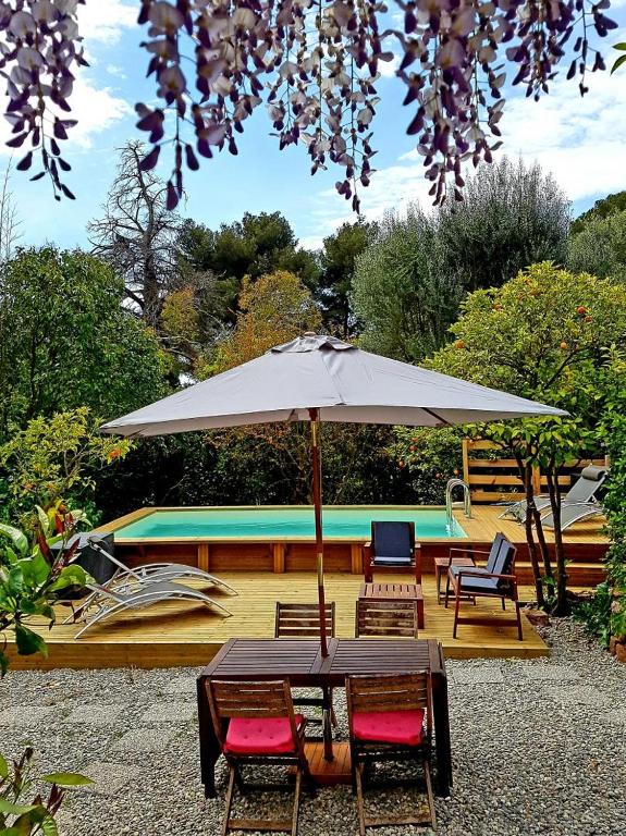 une table avec un parasol devant une piscine dans l'établissement Gite de l'eolienne, à Carqueiranne