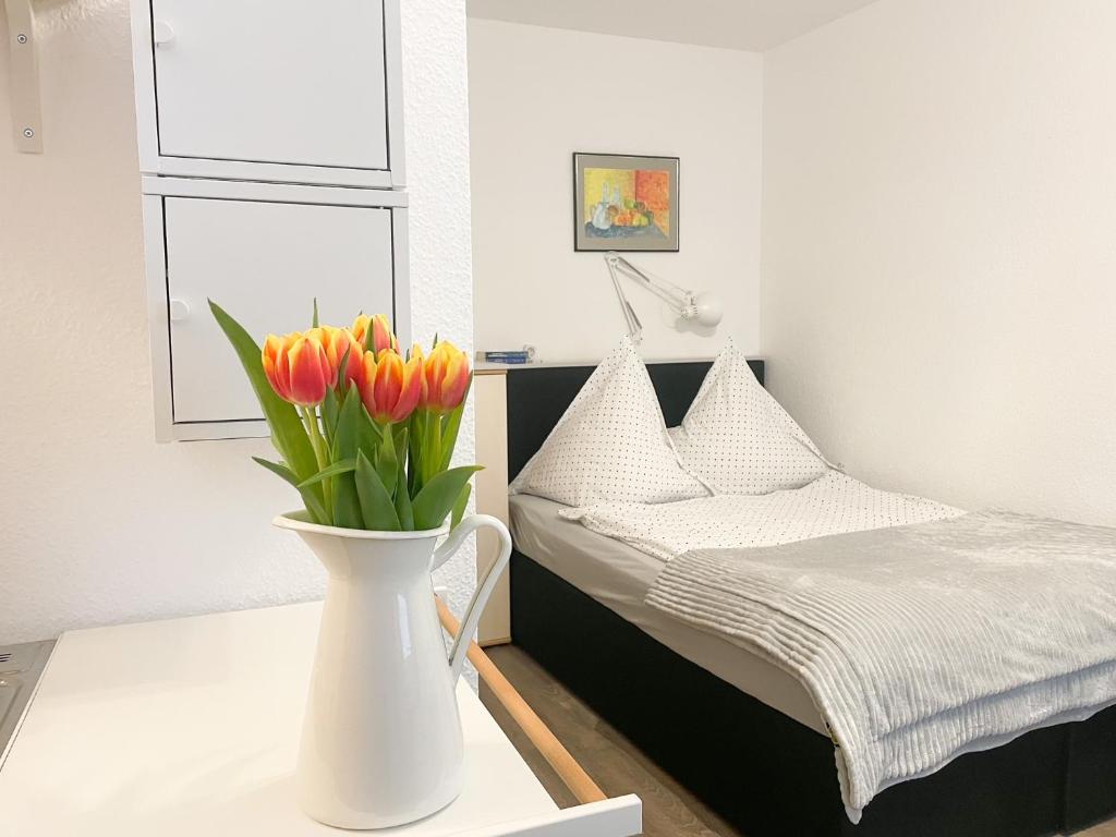a white vase with flowers on a table next to a bed at Ferienzimmer Adalonia in Greifswald