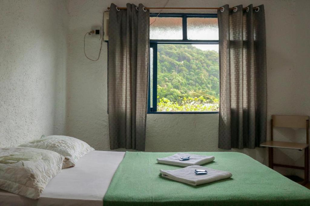 a bedroom with a bed with a green blanket and a window at Pousada Casa da Penha in Abraão