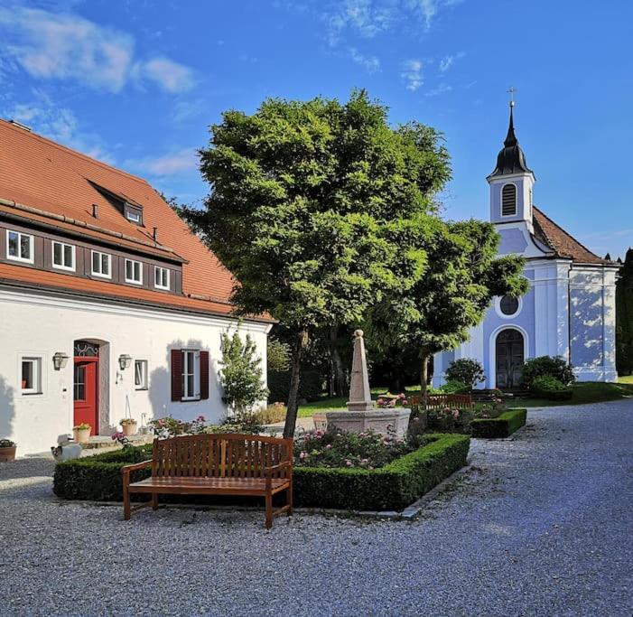 eine Kirche mit einer Bank und einem Baum davor in der Unterkunft Ferienwohnung Gutshof in Seenähe in Dießen am Ammersee