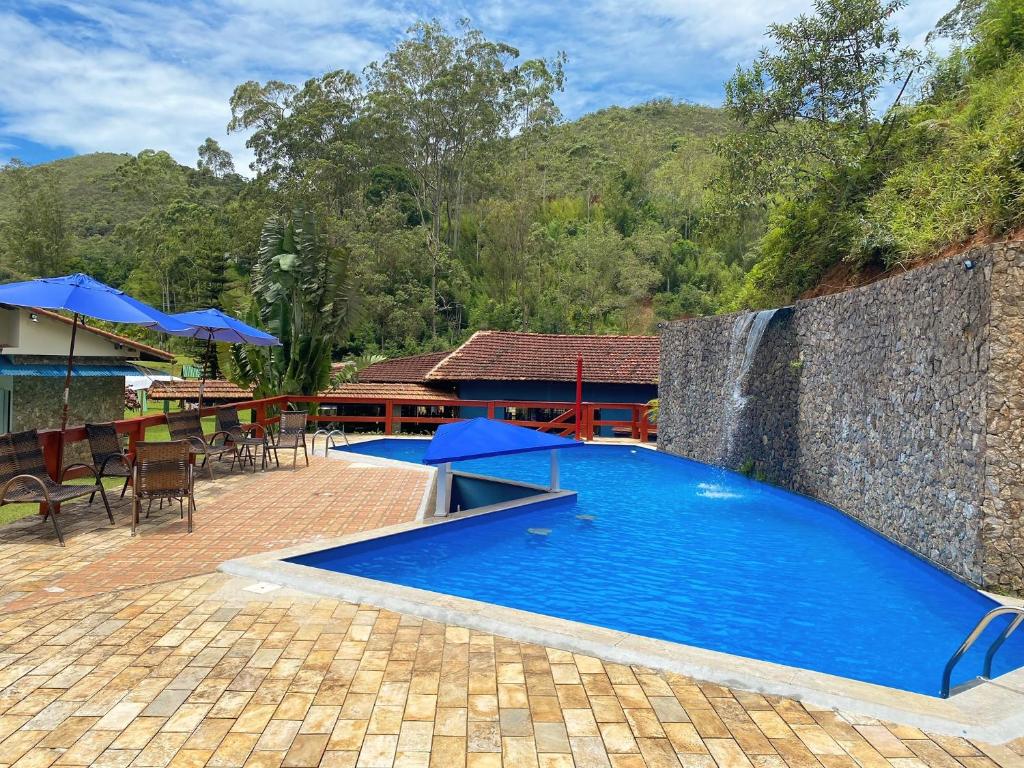 basen z niebieskimi parasolami obok budynku w obiekcie Hotel Fazenda Bonanza w mieście Engenheiro Paulo de Frontin
