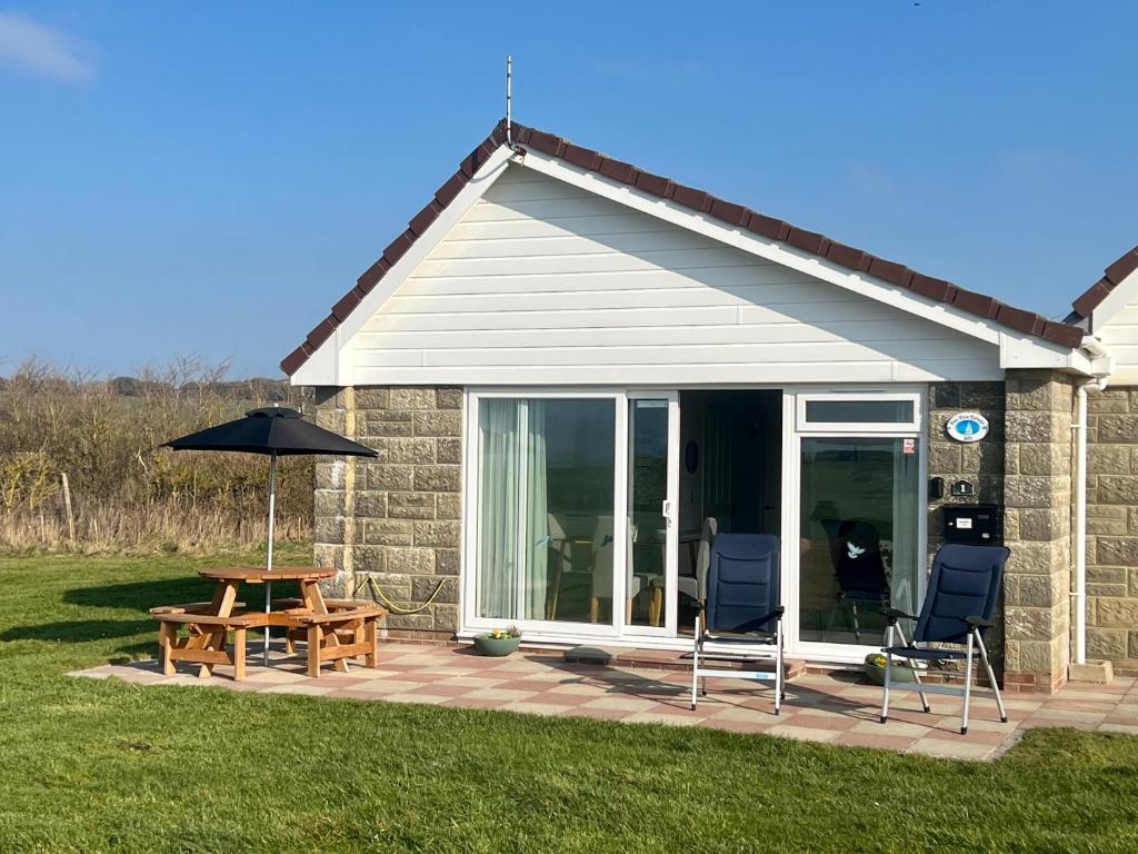 een patio met een tafel en stoelen en een parasol bij BAYVIEW self-catering coastal bungalow in rural West Wight in Freshwater