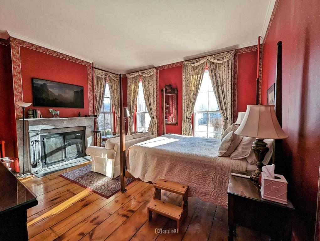 um quarto com paredes vermelhas, uma cama e uma lareira em Cromwell Manor Inn em Cornwall-on-Hudson