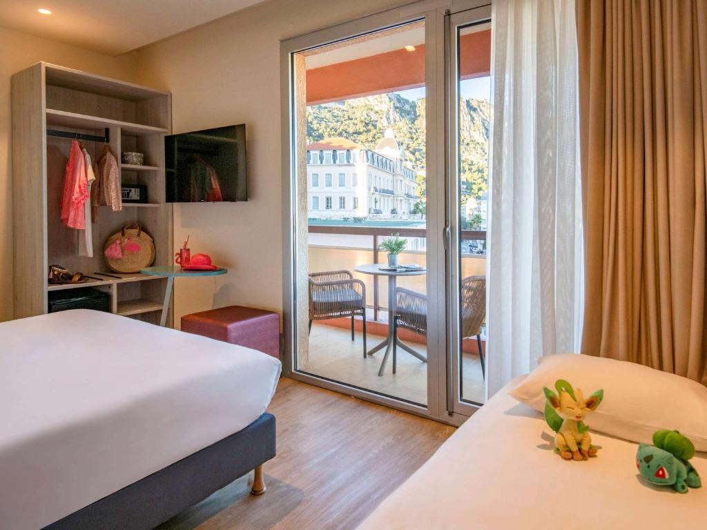 a bedroom with a bed and a balcony with a table at ibis Styles Beaulieu sur Mer in Beaulieu-sur-Mer