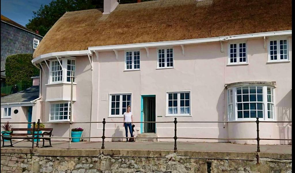 una mujer parada frente a una casa blanca en Benwick Cottage - Beachfront Thatched Cottage set on the marine parade with absolutely spectacular Sea views! Sleeps 4, en Lyme Regis