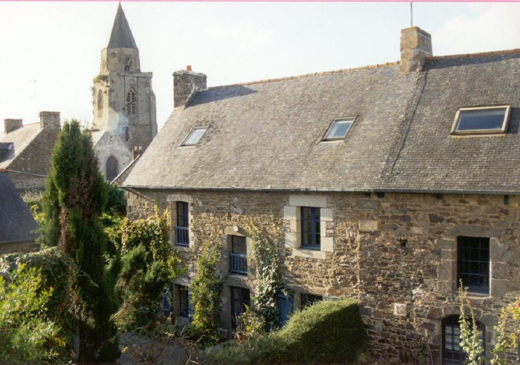 une ancienne maison en pierre avec une église en arrière-plan dans l'établissement La Goëlette, à Saint-Suliac