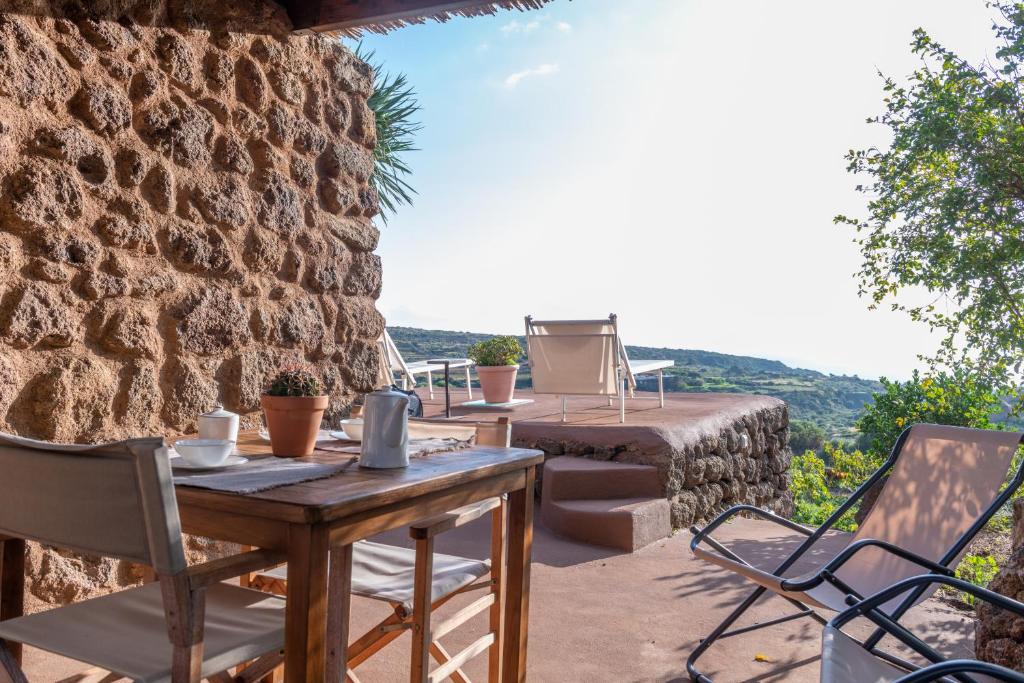 een patio met een tafel en stoelen en een stenen muur bij Dammusi IL SERRALH -Pantelleria- in Pantelleria