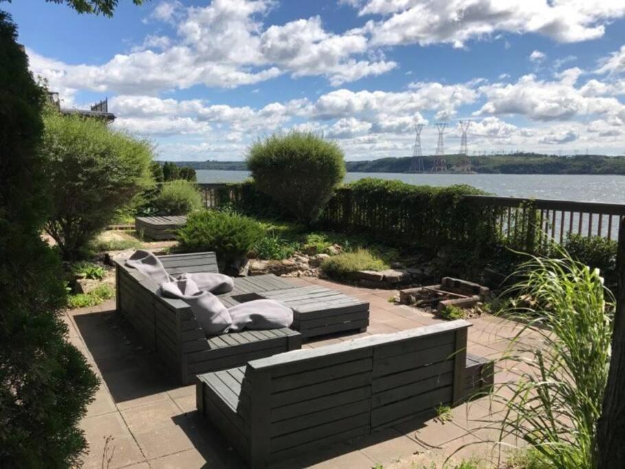 un banco con almohadas sentado en un patio con vistas al agua en Om chalet 2 avec spa et foyer bordé du fleuve, en St-Pierre-de-l'Île-d'Orléans