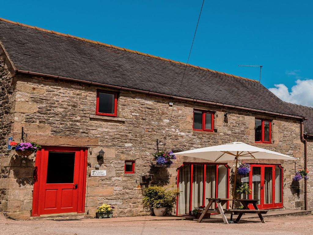 - un vieux bâtiment en pierre avec des portes rouges et un parasol dans l'établissement Cedar Cottage - Rchp132, à Calton