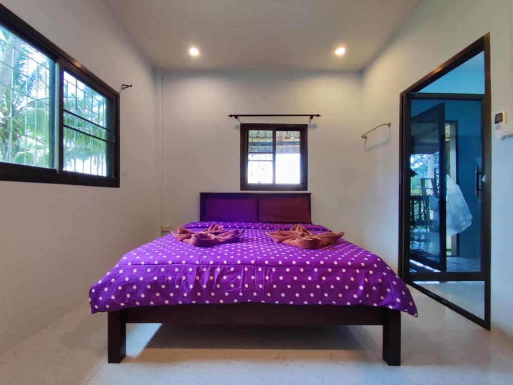 a purple bed in a room with two windows at Chalisa Bukit House Lanta in Ban Mo Nae
