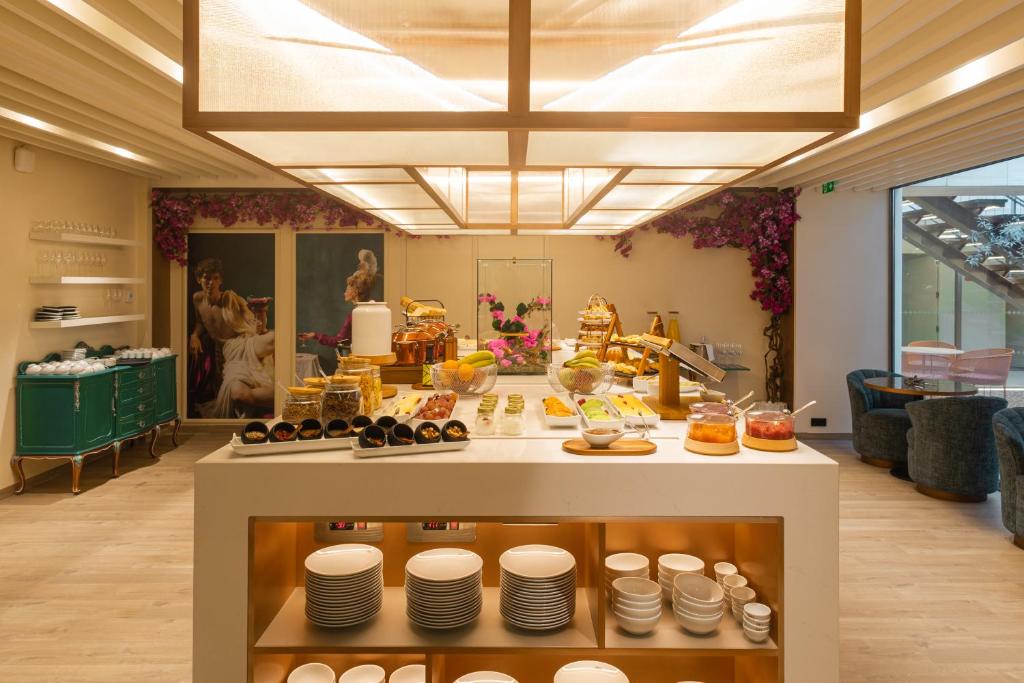 A full breakfast room with a central buffet island, crockery storage, pastries, preserves, and seating by glass walls.