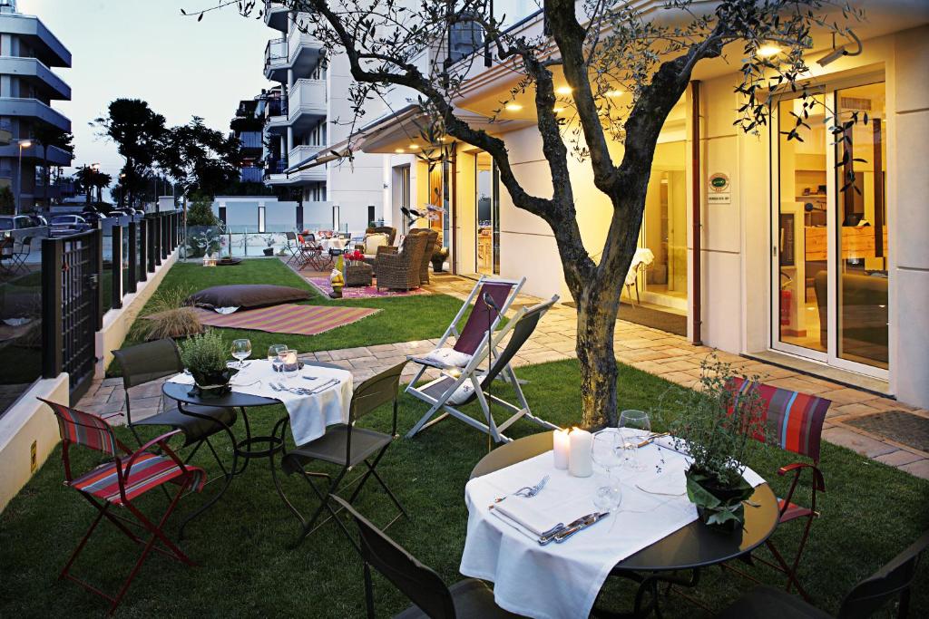 un patio con 2 tavoli, sedie e un albero di D-Place Hotel & Suite a Riccione