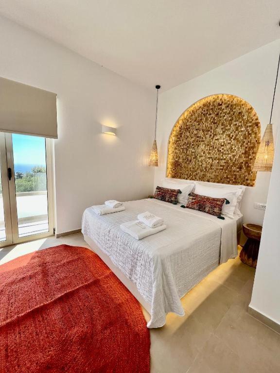 a white bedroom with a large bed with a red rug at Thealos Santorini ( close to square) in Pirgos