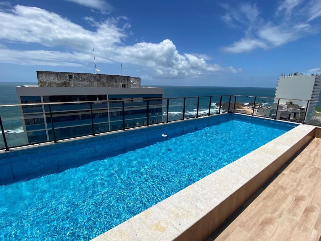 uma piscina no topo de um edifício com o oceano em Apartamento luxuoso a poucos metros da praia em Salvador
