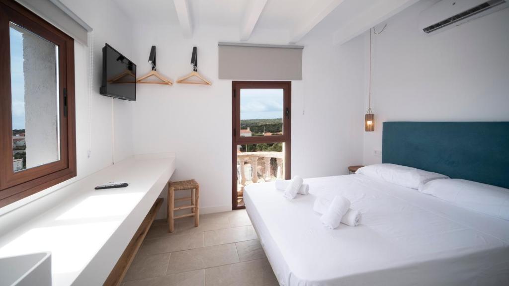 a white bedroom with a large white bed and a window at Castell de Lô in Cala en Porter