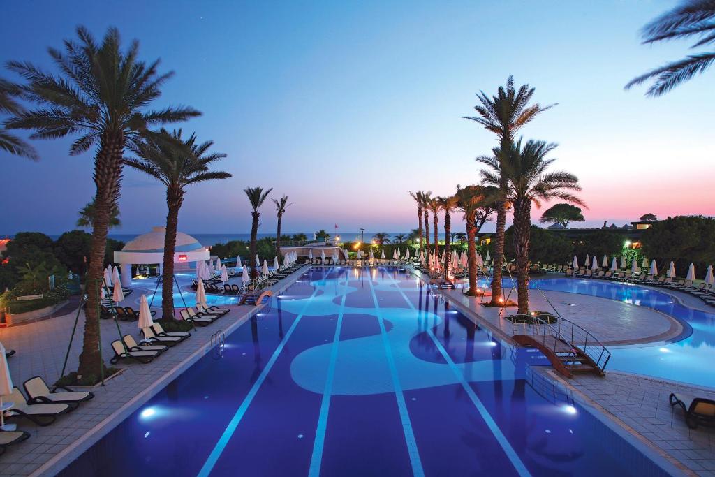een groot zwembad met palmbomen en stoelen bij Limak Atlantis Deluxe Hotel Belek in Belek