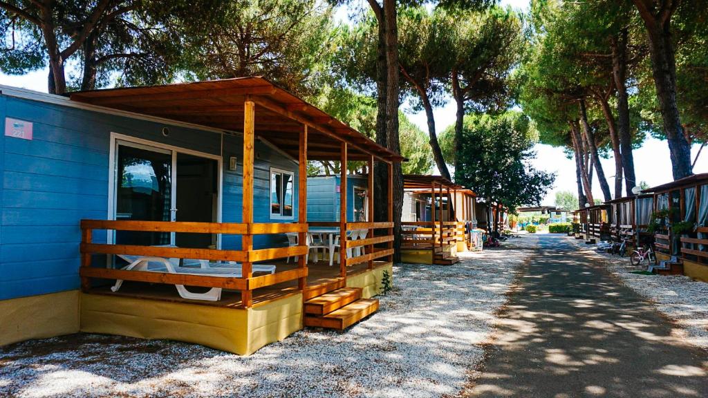 una pequeña casa azul con porche y árboles en Chalet Grand Charme voor 4 personen op Camping River Village - JoyCasa en Ameglia