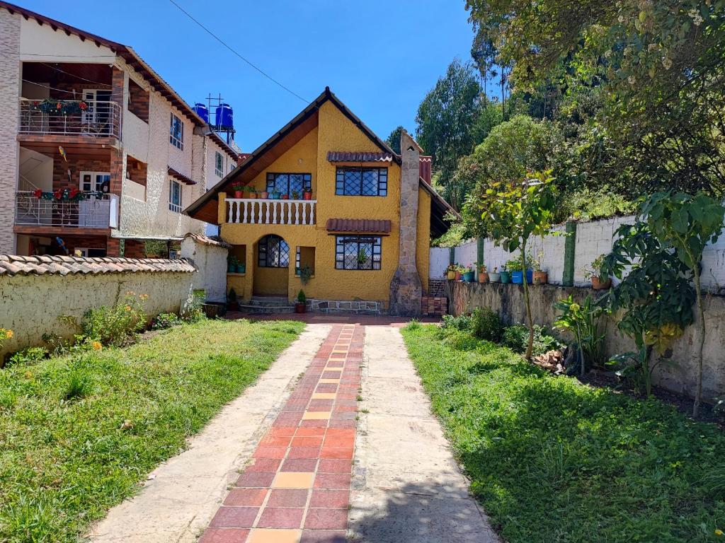 a yellow house with a brick walkway in front of a yard at Alojamiento Chalet - Monguí in Monguí