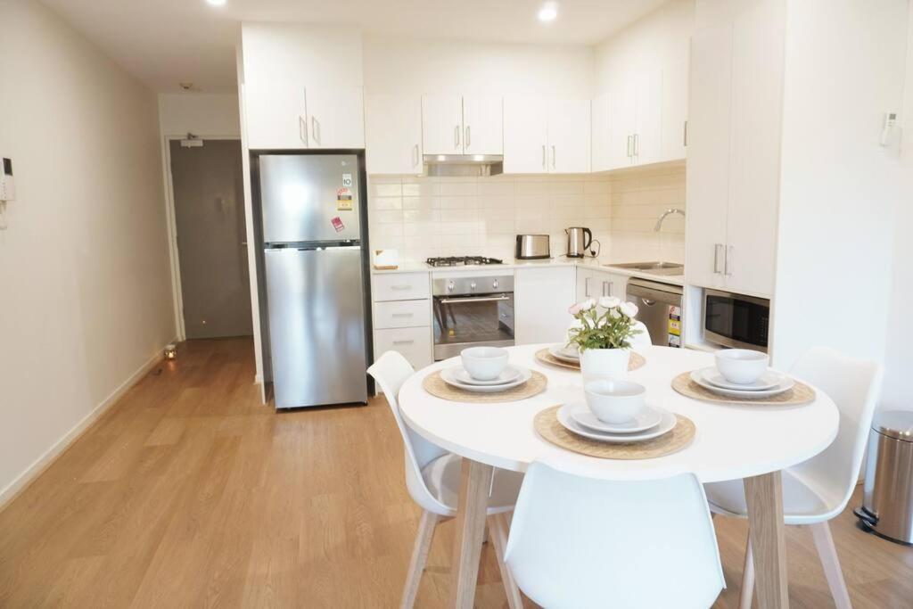 cocina con mesa blanca, sillas y nevera en ViQi Two bedroom apartment front of century walk Including Premium NETFLIX & Prime AMAZON with 75 INCH TV, en Glen Waverley