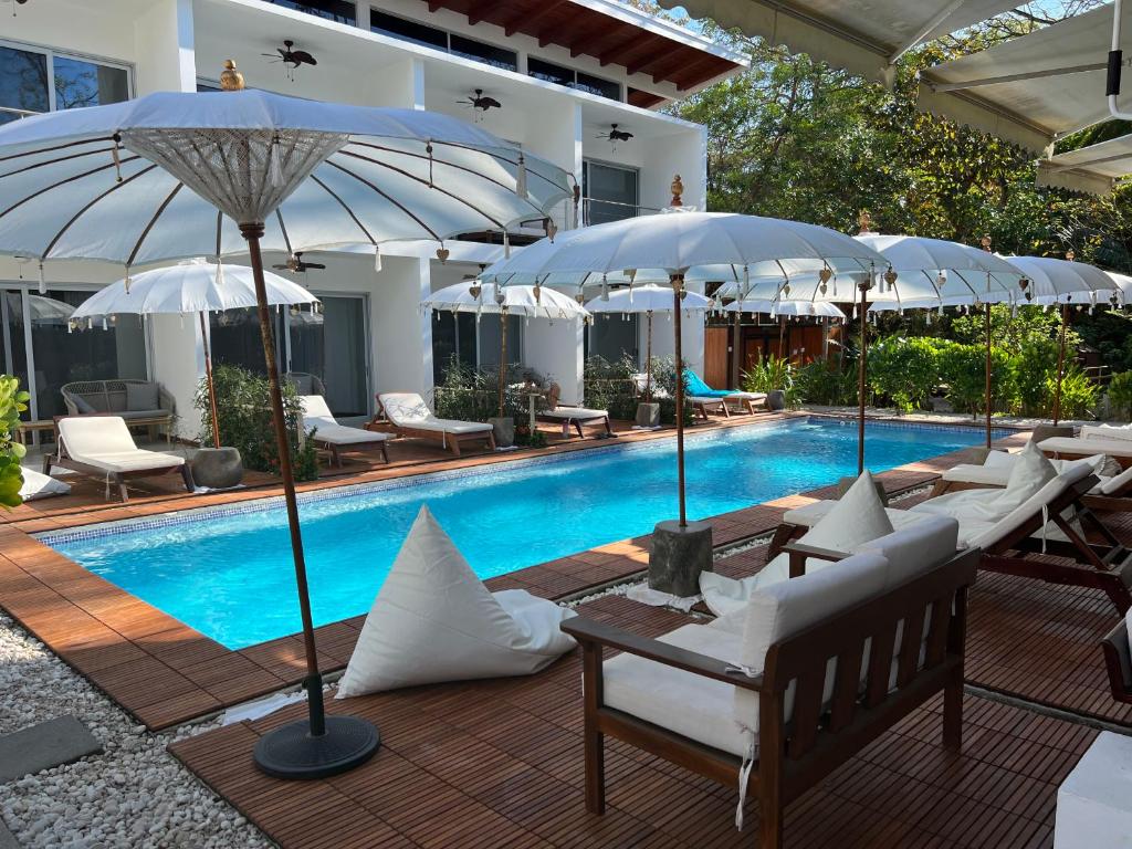 una piscina con sillas blancas y sombrillas junto a una piscina en Ride On Beach House, en Nosara