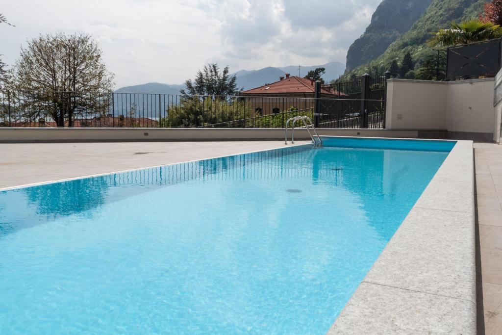 a large blue swimming pool with mountains in the background at Andalero - Palazzo Castelli in Menaggio