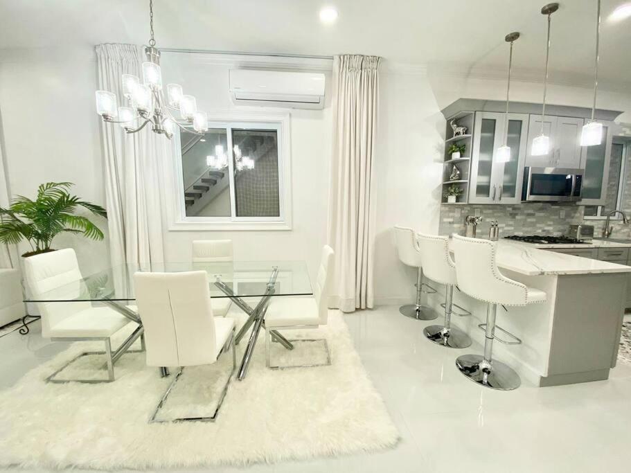 a white kitchen with a glass table and white chairs at Moss Manor in Marsh Harbour