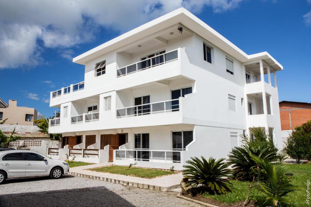 um edifício branco com um carro estacionado na frente em Apartamentos Praia Campeche 50m do mar em Florianópolis