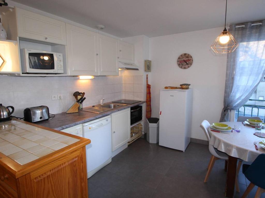 une cuisine avec des placards blancs, un réfrigérateur blanc et une table dans l'établissement Appartement Centre Luchon, 6 pers, Proche Thermes, Balcon, Parking - FR-1-313-150, à Luchon