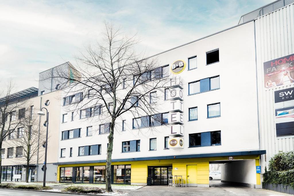 ein weißes Gebäude mit einem Baum davor in der Unterkunft B&B Hotel Bonn-West in Bonn