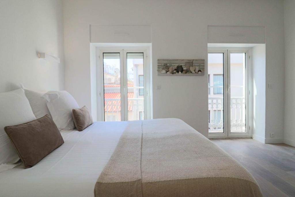 a white bedroom with a large bed and two windows at NAPOLEON Luxurious renovated apartment 1min from Palais in Cannes