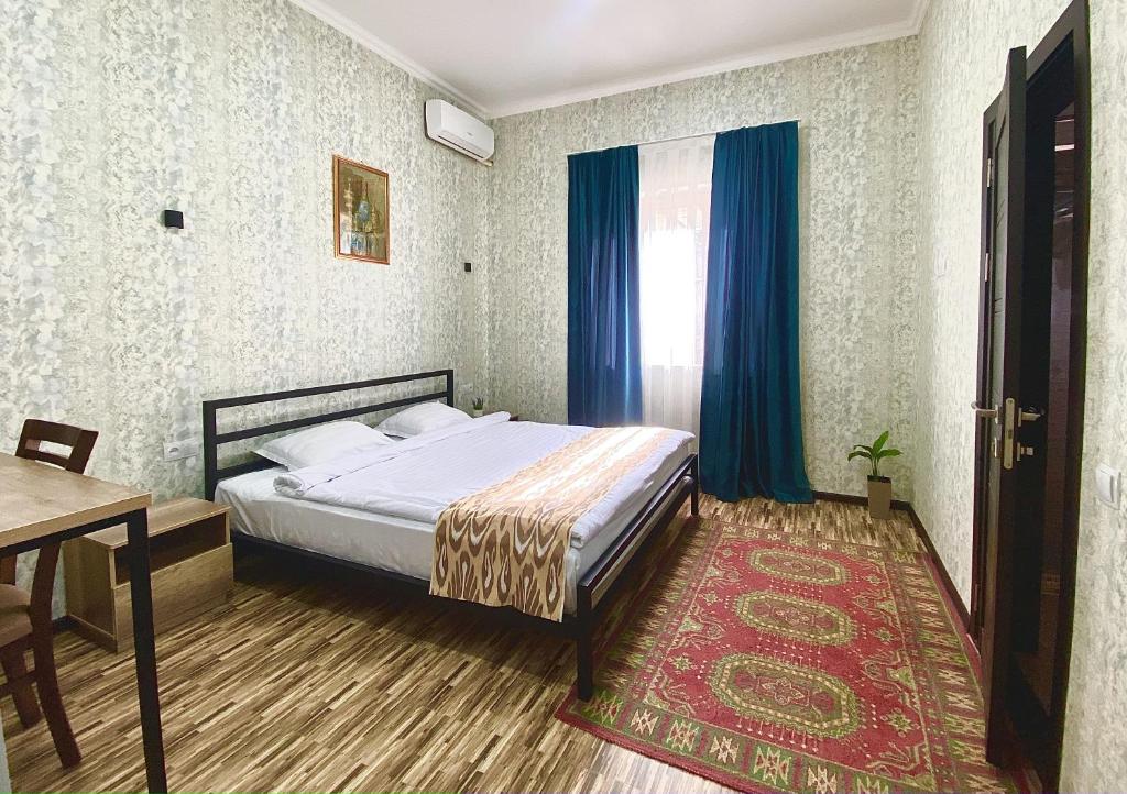 - une chambre avec un lit avec des rideaux bleus et une table dans l'établissement Zahid Inn, à Tachkent