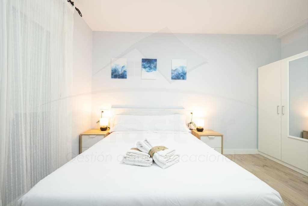 a white bedroom with a large bed with two tables at Cruz Victoria By Silastur in Gijón