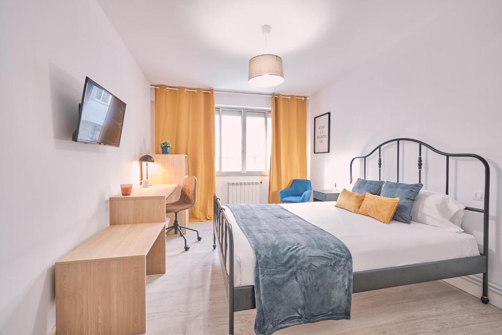 Schlafzimmer mit einem Bett, einem Schreibtisch und einem TV in der Unterkunft Dadá Coliving & Rooms by Serendipia Turismo in Santiago de Compostela