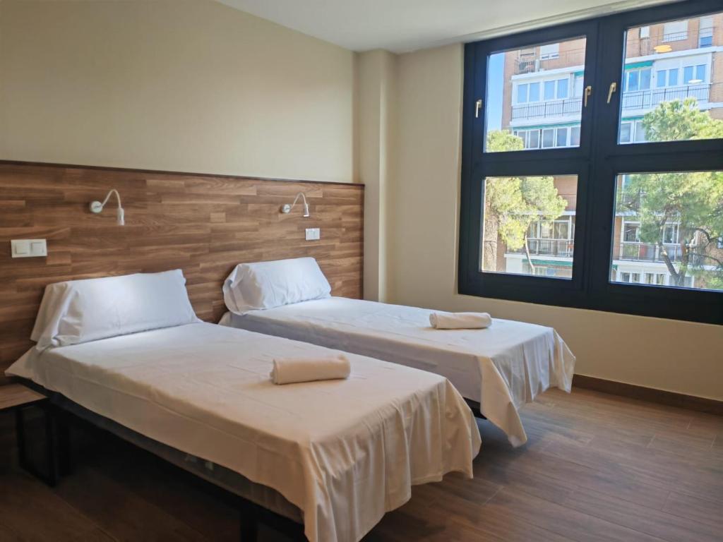 two beds in a room with two windows at Apartahotel Golden Alcalá in Alcalá de Henares