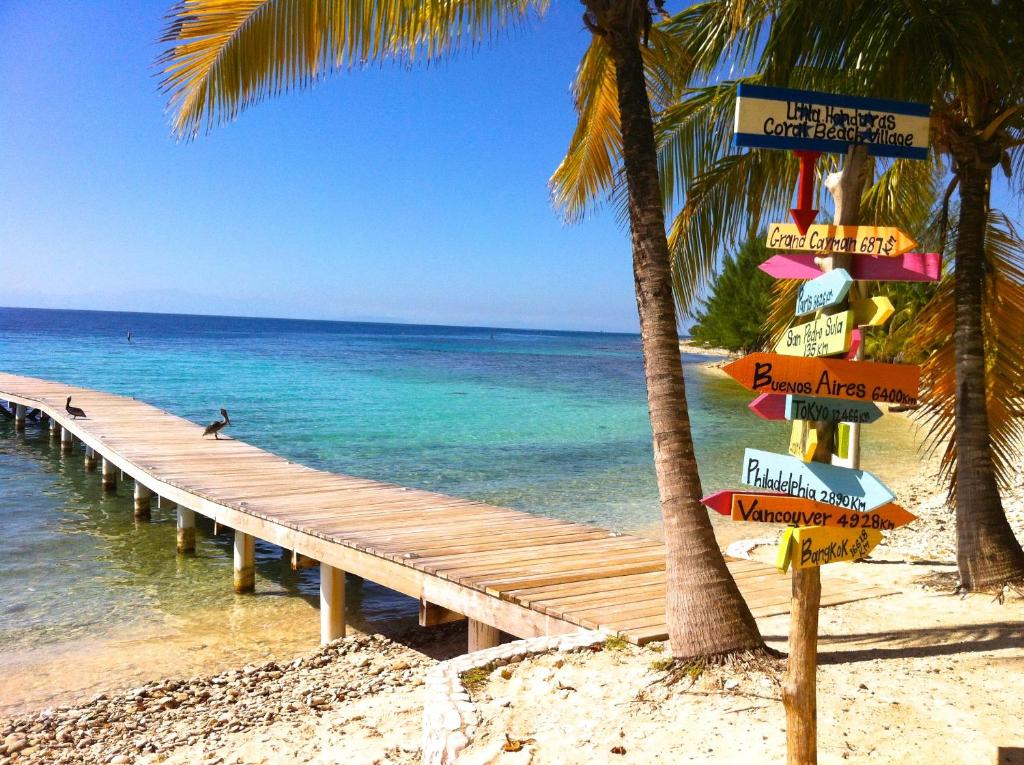 a pier with signs on the beach next to the ocean at Coral Beach Village Resort in Utila