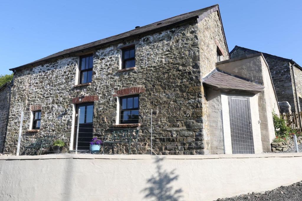 - un bâtiment en pierre avec des fenêtres au-dessus d'un mur dans l'établissement Ponycob hot tub 2 bed ensuite, à Llwyn-Dafydd