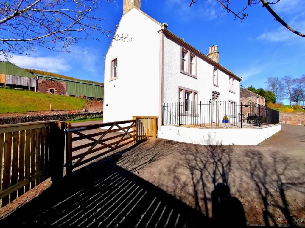 a white house with a fence in front of it at Balmeadowside Farmhouse with Hot Tub in Cupar