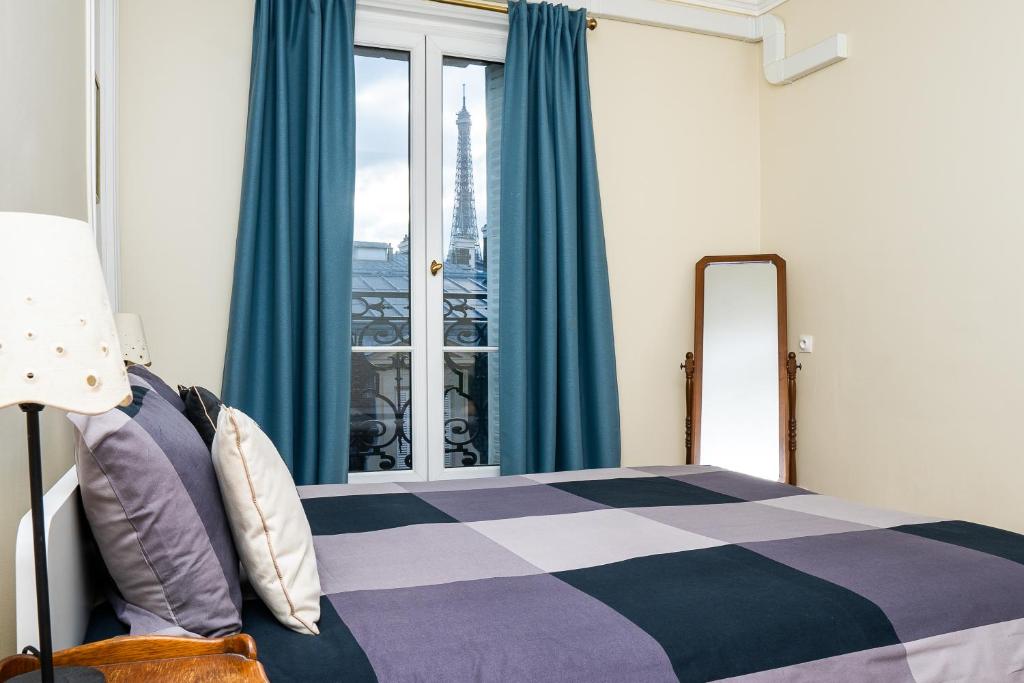 a bedroom with a bed with blue curtains and a window at Eiffel Tower view Residence in Paris