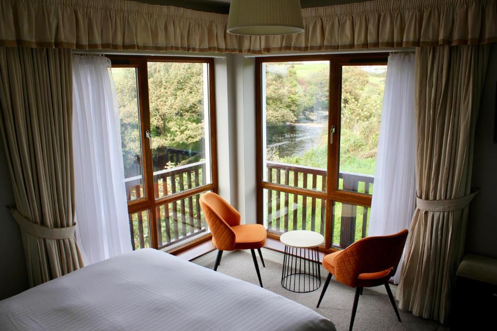 a bedroom with a bed and two chairs and a balcony at Riverbank Rooms in Doolin