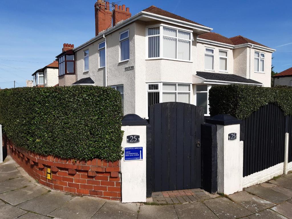 una casa blanca con una puerta negra y una valla de ladrillo en Blackpool Abode - Caxton Lodge en Blackpool